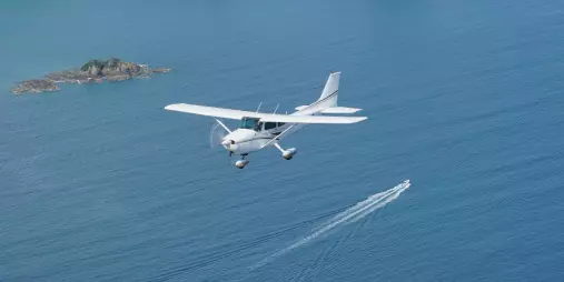 Light aircraft flying over the Hauraki Gulf near Waiheke Island on a scenic flight from Auckland, with a boat visible below.