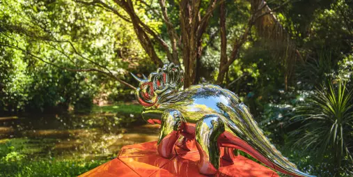 Shiny metallic triceratops sculpture on red geometric base by Gregor Kregar at Brick Bay, Auckland