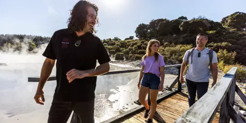 Visitors cross a wooden bridge through steam clouds during a geothermal walk at Hell’s Gate Rotorua.