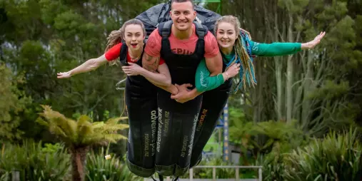 Three people hanging in flight suits before swinging on the Swoop ride in Rotorua