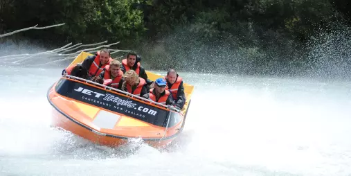 Jet boat performing a high-speed power slide on the Waimakariri River with water spray