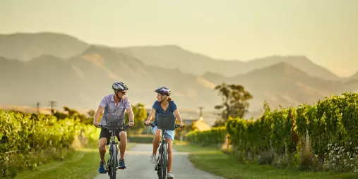 Couple cycling through Marlborough vineyards at golden hour on a self-guided wine tour