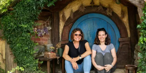 Two women sitting at a blue round door on the Hobbiton Movie Set tour in Matamata, New Zealand