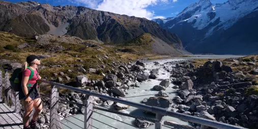 Woman hiking across a swing bridge on the Hooker Valley Track in Aoraki Mount Cook National Park
