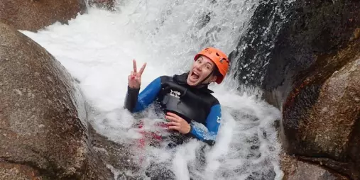Canyoner sitting in a natural water chute giving peace sign in Torrent River canyon