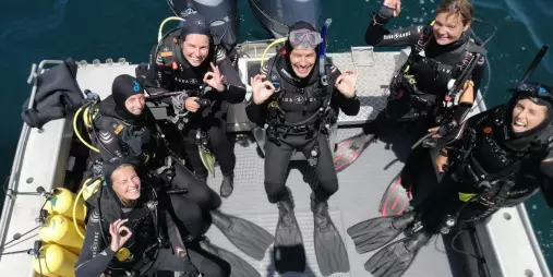 Group of scuba diving students giving OK signs on a boat in Northland, New Zealand