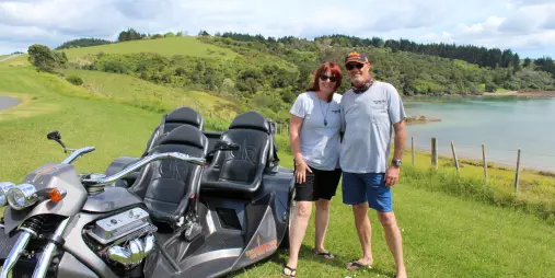 Thunder Trike owners posing by their custom trike near a scenic coastal lookout in Northland