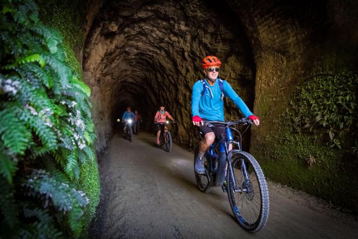 Group of cyclists riding through a rocky tunnel on the Clutha Gold Cycle Trail in Central Otago, New Zealand