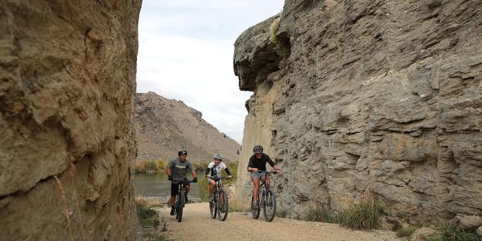 Three cyclists riding through the rocky landscape of the Roxburgh Gorge Cycle Trail near Alexandra in Central Otago, New Zealand