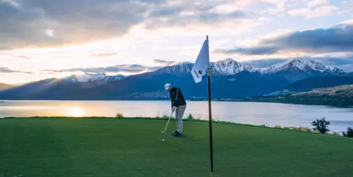 Golfer putting at Jack’s Point Golf Course in Queenstown with Lake Wakatipu and snow-capped mountains at sunset