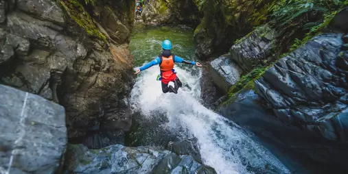 A canyoner leaps into a pool below from the top of a waterfall between sheer canyon walls.