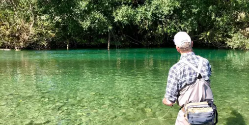 Fly fisherman casting in a crystal-clear river near Queenstown