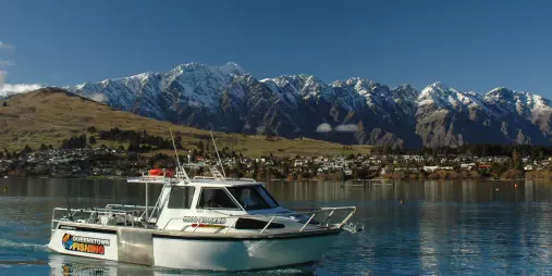 Fishing boat with Queenstown Fishing branding on Lake Wakatipu with snowy mountains in the background