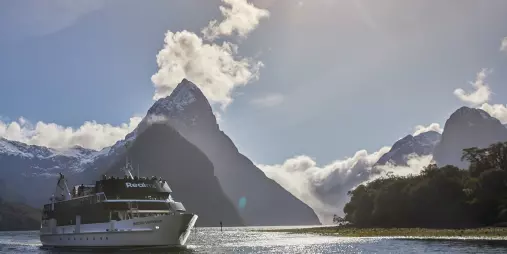 Sovereign vessel cruising Milford Sound with sun flare over Mitre Peak