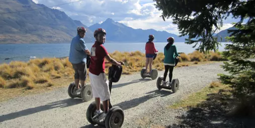 Segway group riding along a gravel track with Lake Whakatipu and mountains in view