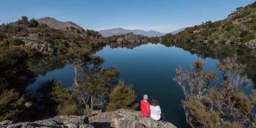 A couple sits peacefully beside the calm waters of Arethusa Pool on Mou Waho Island.