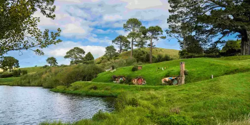 Lush green hills and Hobbit holes set along a peaceful lakefront at the Hobbiton Movie Set in New Zealand