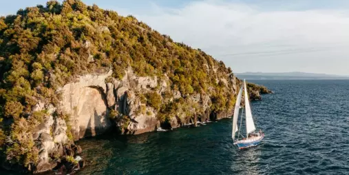 Sailboat cruising past the forested cliffs of Mine Bay on Lake Taupō