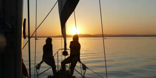 Two people silhouetted on the bow of Kindred Spirit during a sunset sail on Lake Taupō