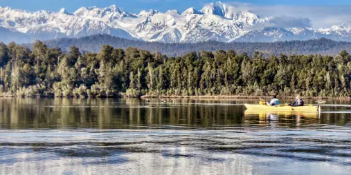 Kayakers paddling on Okarito Lagoon with snow-covered Southern Alps in the background